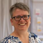 Portrait Sabine Ayeni. Sie hat kurze graue Haare und trägt eine schwarze Brille.