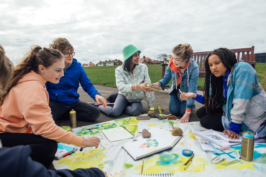 Eine Gruppe Jugendlicher gestalten mit verschiedenen Bastelmaterialien nachhaltige Kunstwerke.